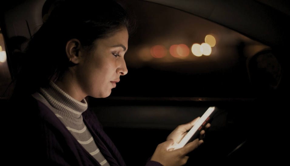 A woman reading her phone in a car at night, city lights behind her